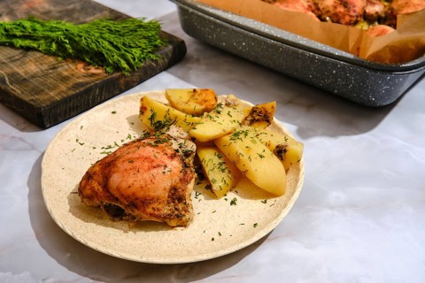 Food is arranged on a plate with roasted chicken and potatoes. Fresh herbs are visible on the food.