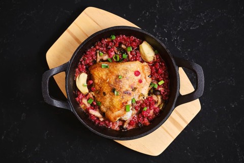 Top view of chicken thigh roasted with lingonberry and garlic. The skillet is placed on a wooden