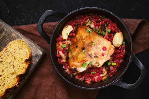 A chicken piece is cooking in a pot filled with lingonberry and garlic. A slice of bread is placed
