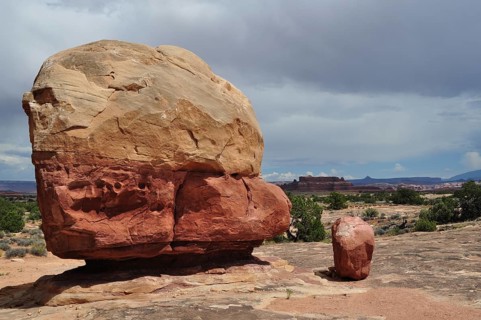 Large round boulder in an open desert landscape under a cloudy sky, Canyonlands National Park,