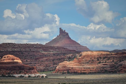 Distinctive pointed rock rises high, surrounded by red rocks and dramatic cloud formations,