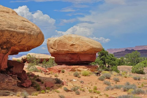 Round rock formations in a vast desert landscape with sparse vegetation and slightly cloudy sky,