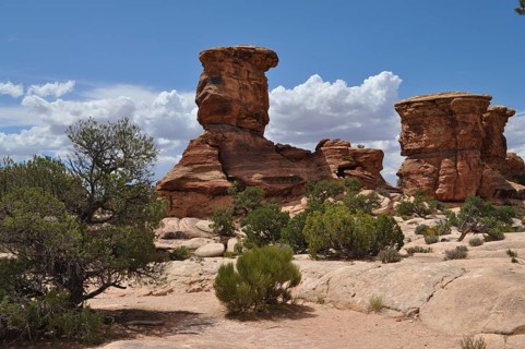 Dramatic rock formations with green shrubs under a blue sky with few clouds in a desert