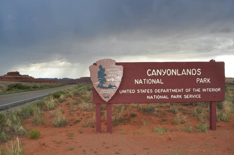 Canyonlands National Park entrance sign under cloudy sky in a dry desert landscape, Canyonlands