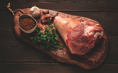 Raw pork knuckle, on a wooden chopping board, with spices, close-up, top view, no people