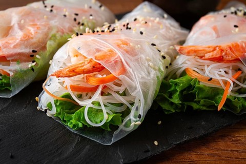 Shrimp rice paper rolls on a black plate with fresh vegetables and sesame seeds