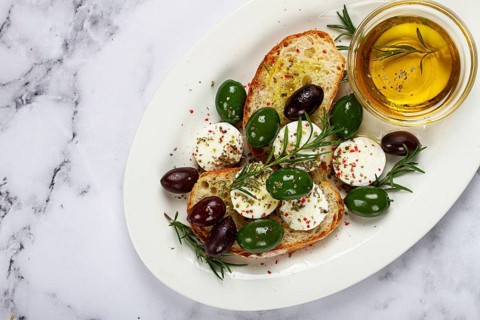 A plate with a snack, ciabatta bread with cheese and olives, olive oil, spices and herbs, top view,