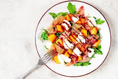 Salad with slices of ripe melon, prosciutto, mozzarella and fresh arugula, decorated with balsamic