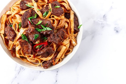 Udon noodles with Mongolian beef, green onions and vegetables, in a white plate, on a light