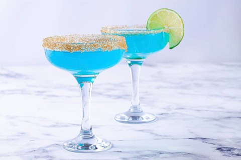 Colorful blue cocktails in elegant glasses with lime garnish on a marble table