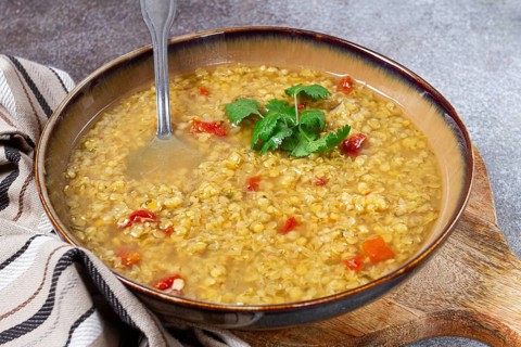 A hearty lentil soup is presented in a rustic bowl, featuring vibrant tomato pieces and fresh