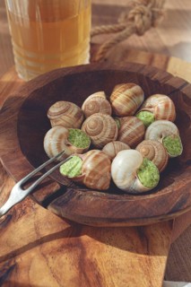 Snails cooked with herb oil on a wooden plate, served with white wine, natural light, no people