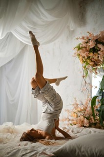 A woman is practicing a yoga pose by balancing on her shoulders with her legs raised. She is on a