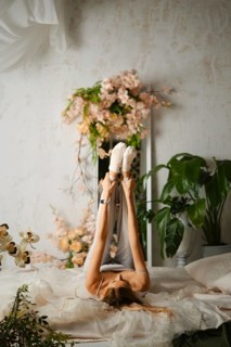 A woman is lying on her back while stretching her legs up in the air. The room has many plants and