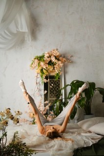 Flexible woman lies on her back with her legs up in the air on a bed. The room is filled with