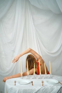 A woman is seen bending gracefully at a table set with candles. The table has white plates and