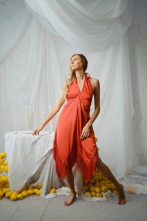 A woman stands near a table covered with a white cloth. She poses in a simple dress. Around her are