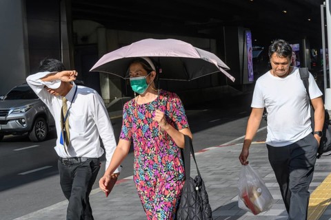 Bangkok, Thailand. March 25th 2025. People shield their faces from the bright sun and wear face