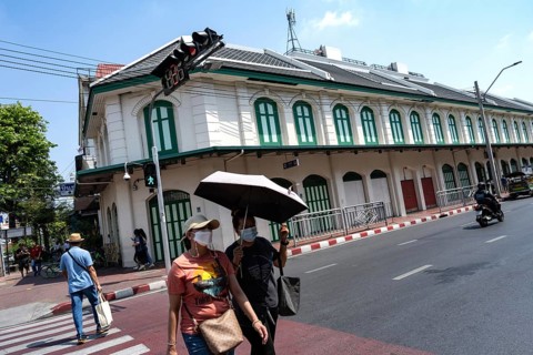 Bangkok, Thailand. March 25th 2025. People crossing the street with masks and an umbrella due to