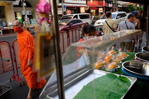 Bangkok, Thailand. February 18th 2025. A Buddhist monk walks past street food stalls along a