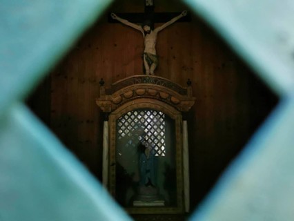 Wooden statue of Jesus on the cross through a grid in a dark chapel, hiking in the Frankenwald