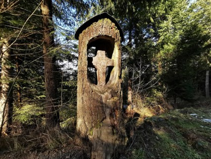 Wooden cross carved into a tree trunk in the forest in a cool atmosphere, hiking in the Franconian