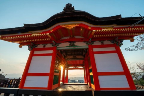Sunset over the city with sun stars, view through the red Nishimon Gate, Kiyomizu-dera Temple, in