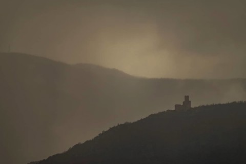The structure is on a mountain. The sky is cloudy and sunlight is shining in the distance. The