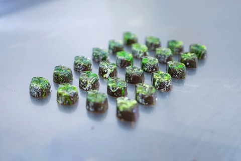 Numerous chocolates with green decorations on a smooth surface, vegan chocolates production,