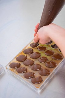 Hand with piping bag fills chocolate into molds on a work surface, vegan chocolates production,