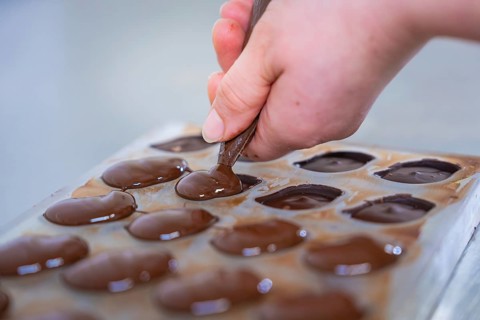 Close-up of filling chocolate molds with chocolate, vegan chocolates production, Haselstaller Hof,