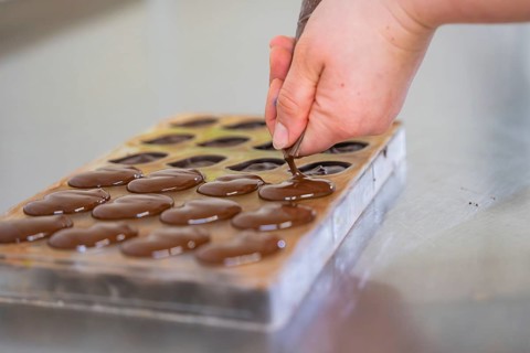 Hand fills chocolate into a chocolate mold lying on a table, vegan chocolates production,