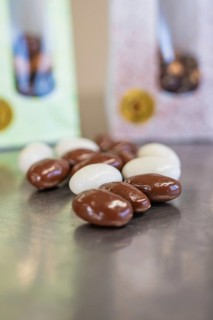 Close-up of white and brown chocolate almonds with packaging in the background, Easter production