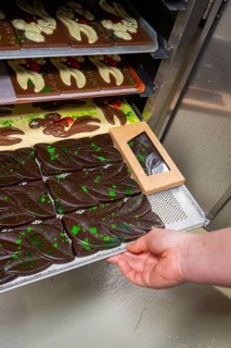 Hand pulls a tray with chocolate bars and chocolates out of the oven, Easter production of regional