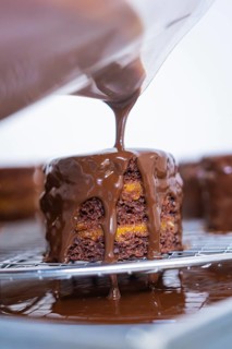 Chocolate coating is poured onto a small cake that is placed on a grid, Vegan Tartchen Production,