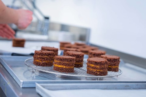 Hands working with small chocolate cakes on a grid in the kitchen, vegan cake production,