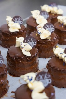Small chocolate cakes with cream and chocolate logo on tray, vegan cake production, Haselstaller