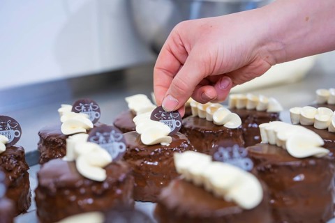Small chocolate cakes are decorated with café logo and white chocolate, Vegan Tartchen Production,