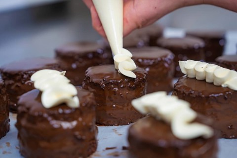 Some chocolate cakes are artfully decorated with cream from a piping bag, vegan cake production,
