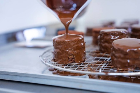 A pastry covered with liquid chocolate drips on a grid in a baking quality kitchen, vegan cake