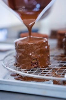 A small pastry is glazed with liquid chocolate and drips off a grid, Vegan Tart Production,