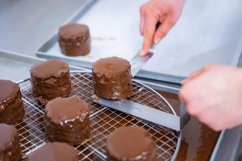 Several small cakes are prepared in the kitchen with shiny chocolate glaze on a grid, Vegan Tarts