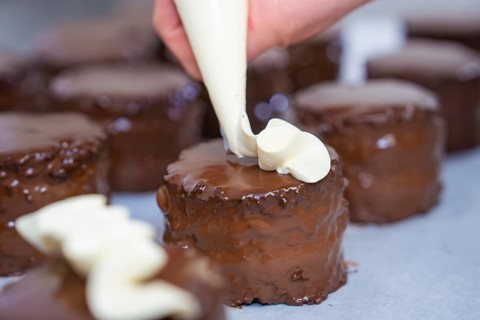 Several chocolate cakes are decorated with cream from a piping bag, Vegan Tart Production,
