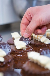 A dessert is decorated with white chocolate and a café logo, Vegan Tart Production, Haselstaller