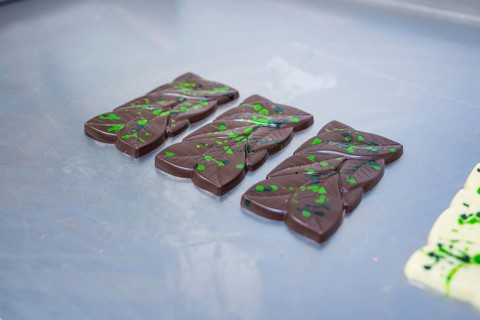 Three dark chocolate bars with green patterns on a table, vegan chocolate production, Haselstaller