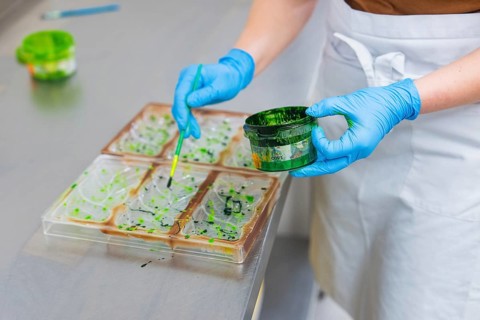 A person in a blue glove paints with a brush from a green paint pot on shapes, vegan chocolate