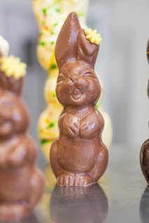 Happy chocolate bunny with flower decoration, standing upright on metal surface, Easter production