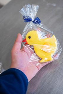 Yellow duck cookie is held in the hand, wrapped in transparent film with blue ribbon, Easter