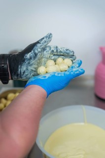 Person holding chocolates over a white bowl in a kitchen, chocolate quail eggs, Easter production,