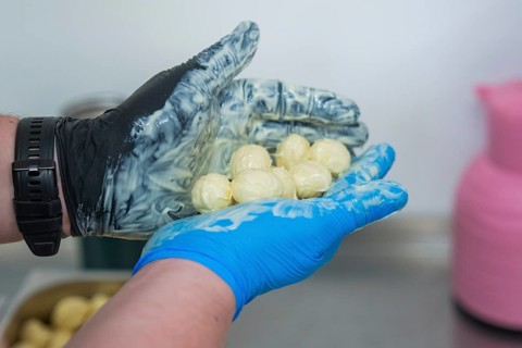 A hand in gloves holds chocolates over a bowl with pink and blue decoration, chocolate quail eggs,